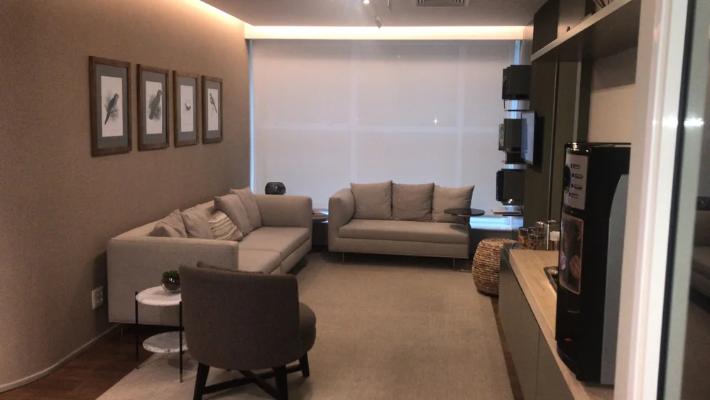 Sala de espera do consultório oftalmológico em tons quentes neutros, com sofás cinza-areia, quadros emoldurados de aves e iluminação suave.