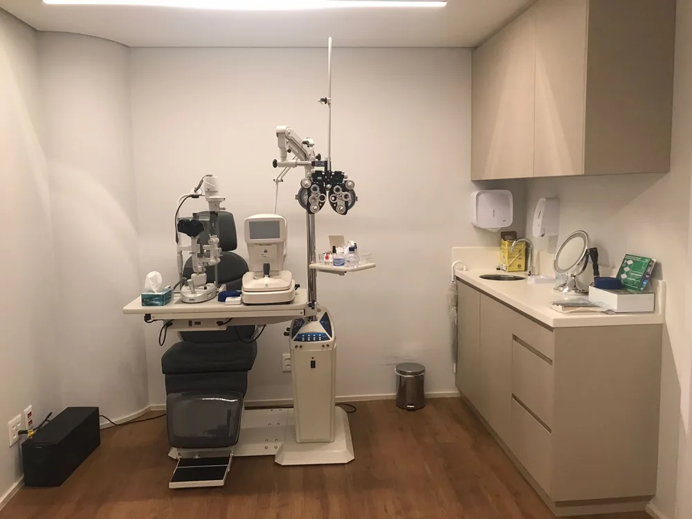Sala de exame oftalmológico equipada com refrator, lâmpada de fenda e autorrefrator.